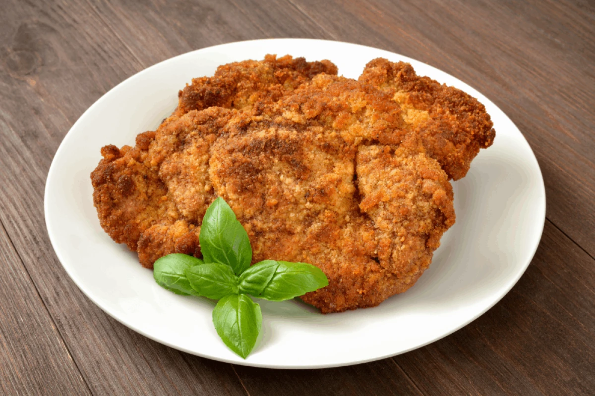 Kotlety schabowe na białym talerzu udekorowane listkiem bazylii